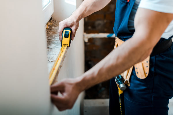 man using a tape measure to measure a window for construction or renovation project 2 critical measurements 2 home improvement tips