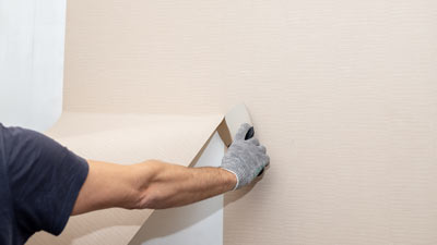 person applying wallpaper to a beige wall using a smoothing tool while wearing gloves home improvement 4 tips