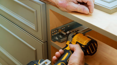 person installing cabinet hardware with power drill on wooden cabinet ten easy steps to improve cabinetry