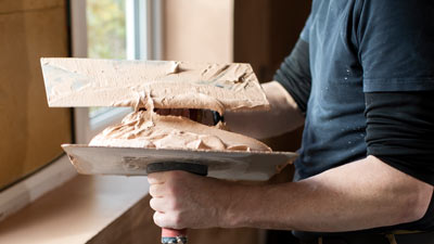 person holding a trowel with plaster near a window applying finishing touches for three steps of renovation