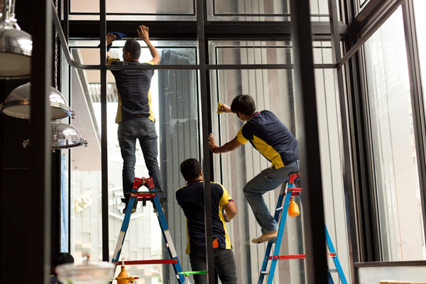 Three workers on ladders cleaning large windows in a commercial space.