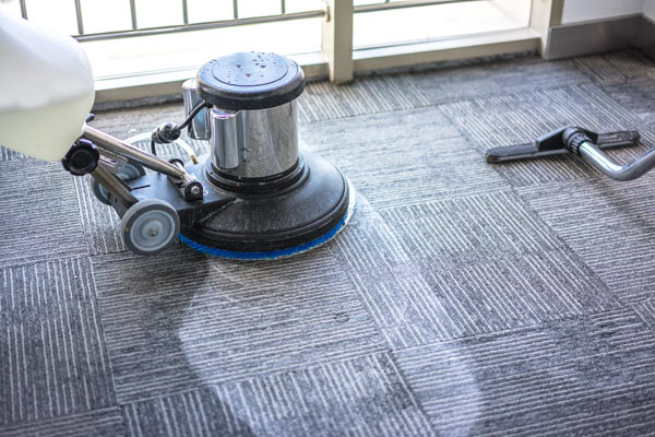 Floor cleaning machine in action on textured carpet tiles, showcasing a shiny clean surface.