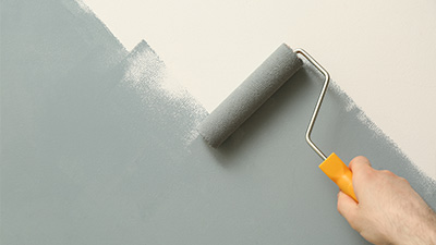 a person using a roller to paint a wall grey